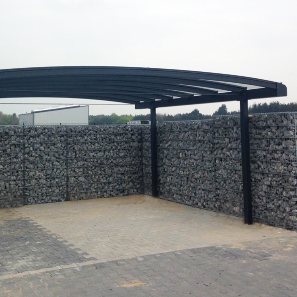 Gebogen aluminium carport met glas. Omheind met schanskorfmuur met grijze stenen.