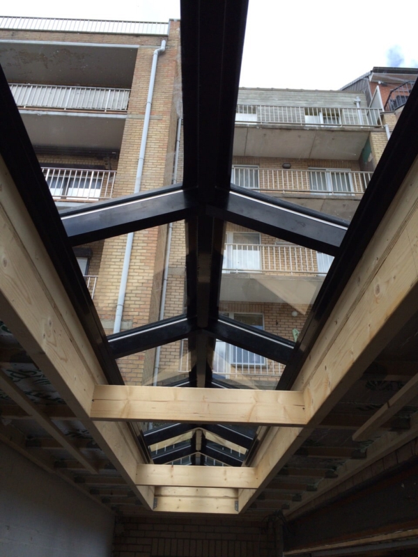 Onderaanzicht zwarte lichtstraat zadeldak boven op plafond met houten balken.