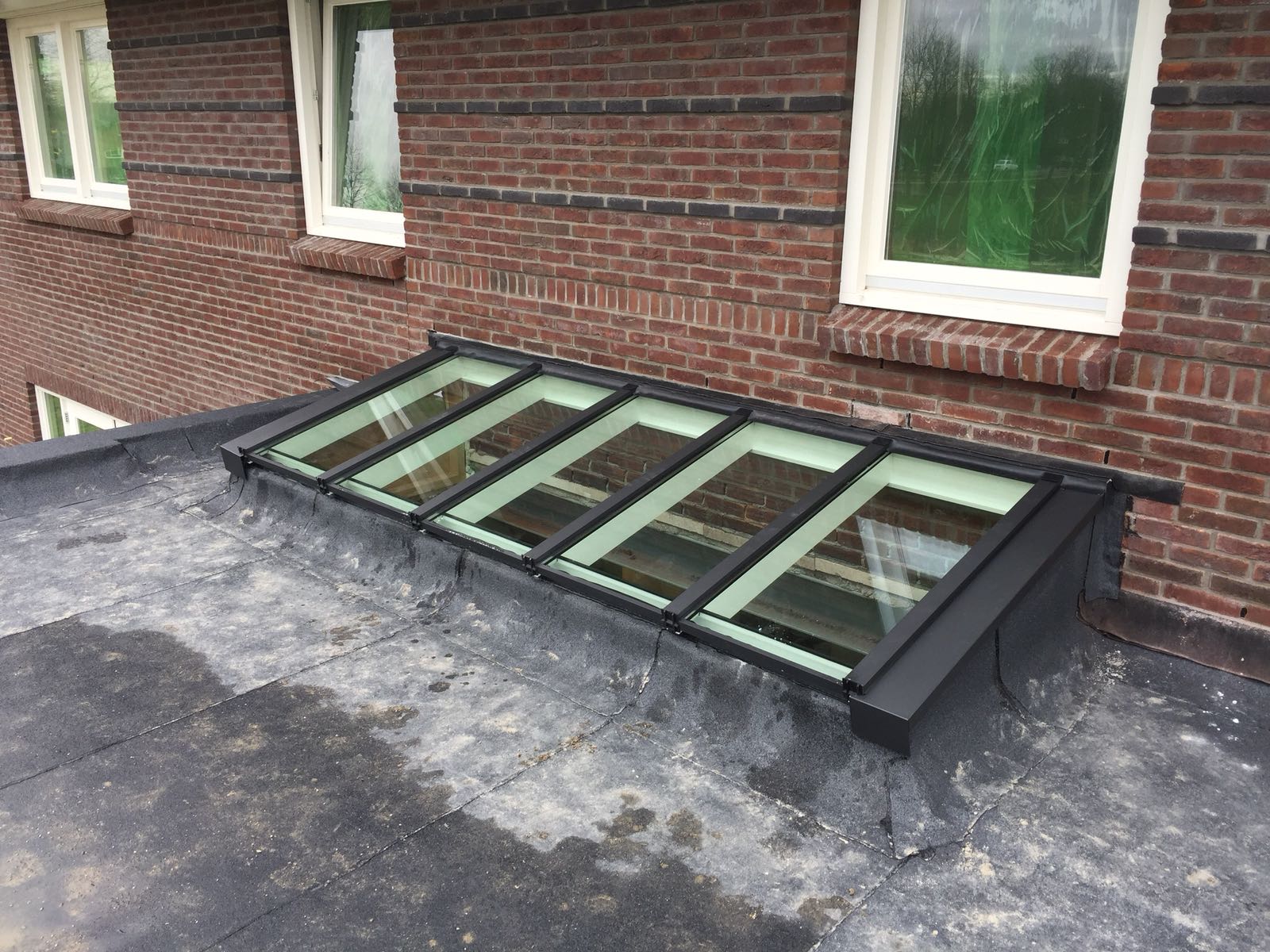 Zwarte lichtstraat lessenaarsdak op plat dak tegen gevel