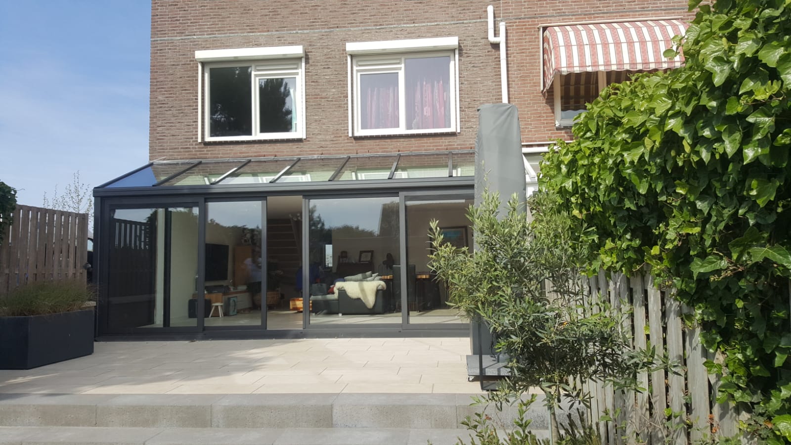 Grijze serre met lessenaars dak en 4-delige schuifpui tegen hoekwoning.