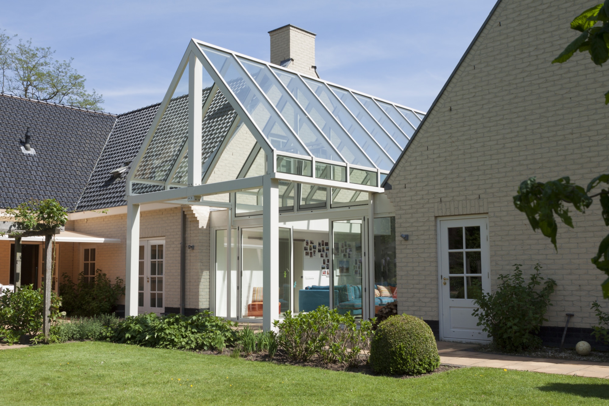Witte serre met zadeldak tussen twee woningen.