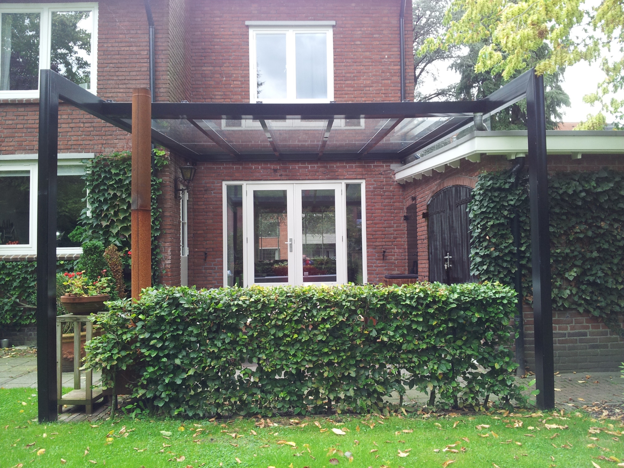 Zwarte terrasoverkapping aluminium maatwerk met glazen dak in de achtertuin