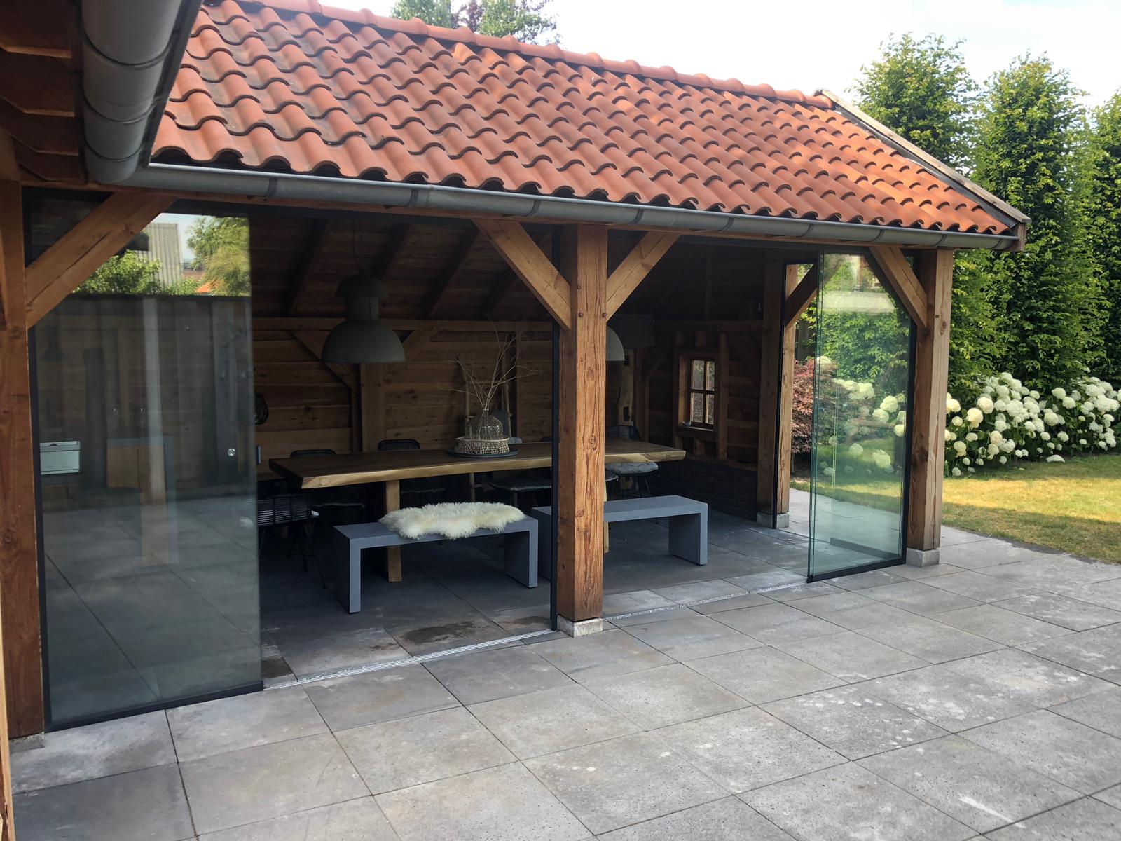 Glazen schuifwand in houten overkapping met puntdak.