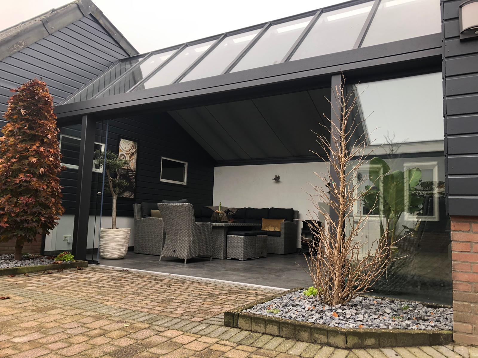 Grijze aluminium tuinkamer met zadeldak en schuifwand tussen twee muren.