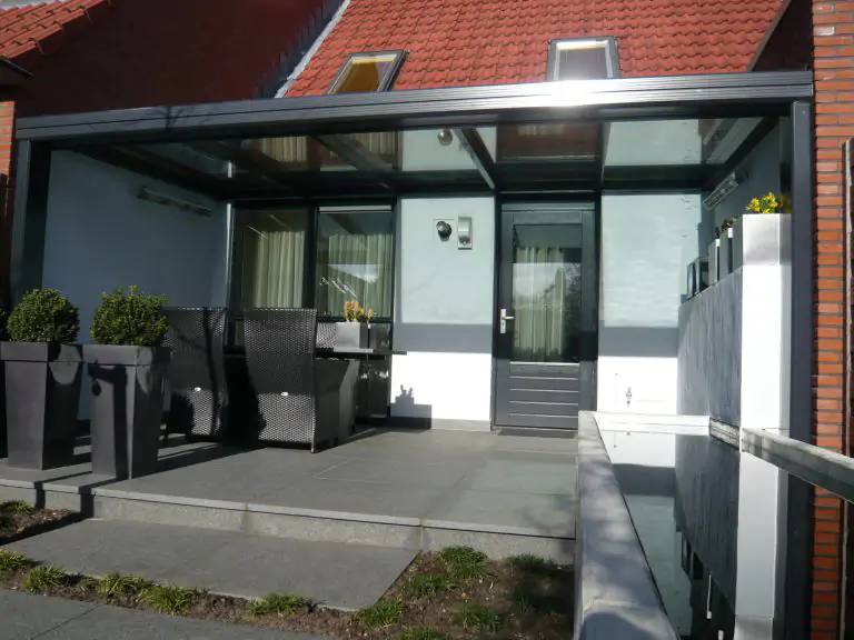 Grijze Aluminium terrasoverkapping met glas en plat dak tegen woning tussen 2 muren.