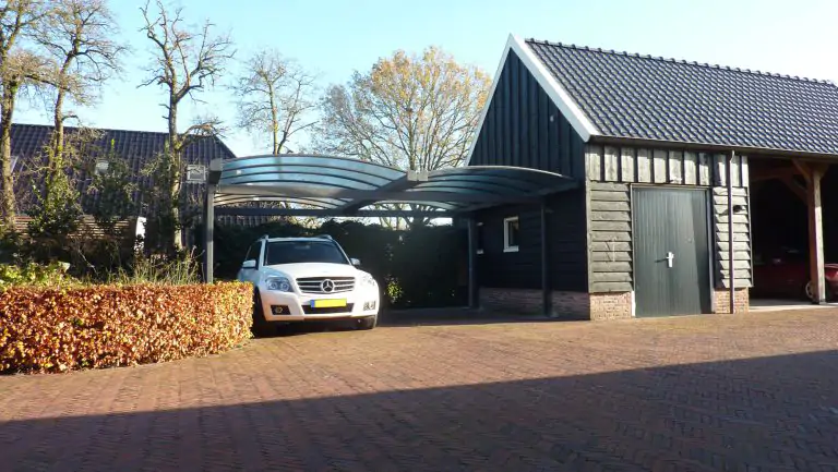 Dubbele gebogen carport met glas naast zwarte houten schuur met witte auto onder de carport