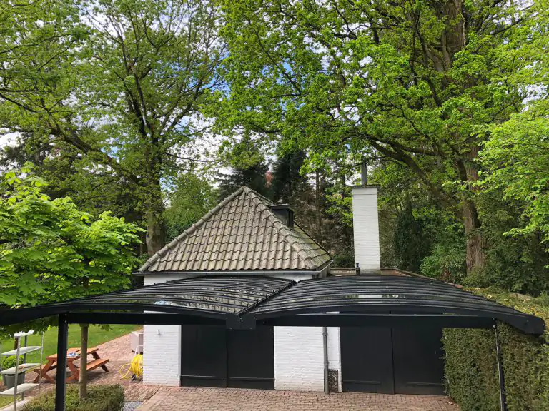 Bovenaanzicht van dubbele gebogen aluminium carport met glas tegen witte stenen garage met groene deuren.