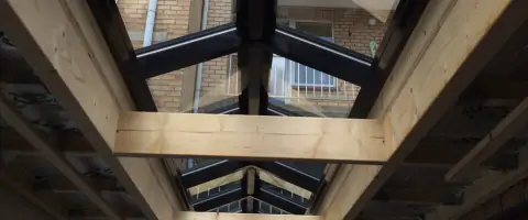 Houten balken en lichtstraat in zadeldak van gebouw.