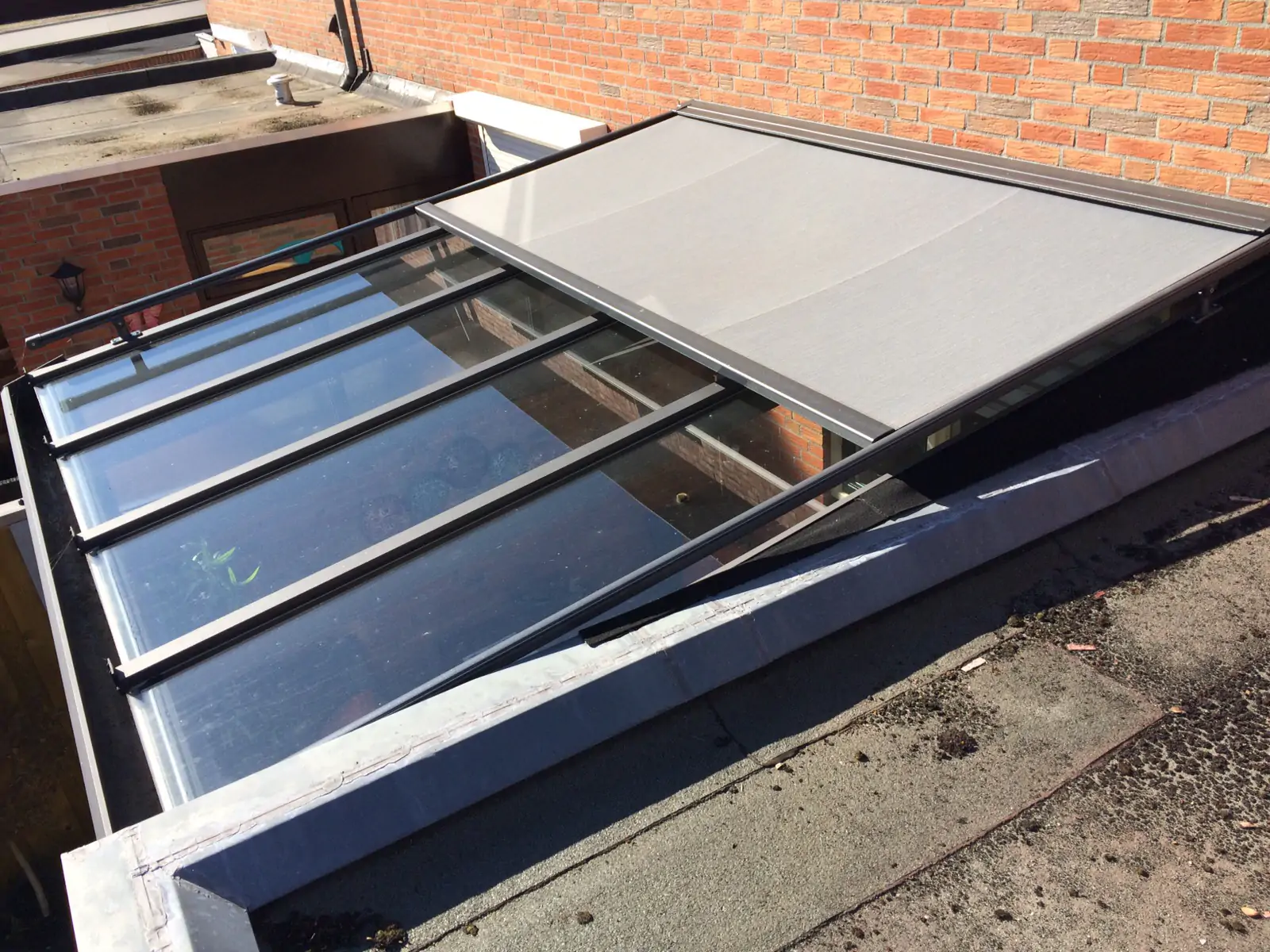 Aluminium lessenaarslichtstraat op een plat dak met buitenzonwering boven het glas.