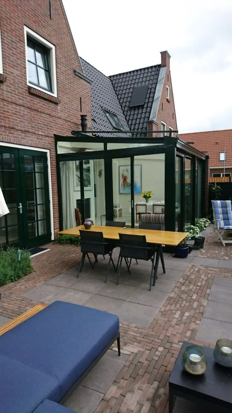 Groene serre met lessenaars dak in achtertuin.