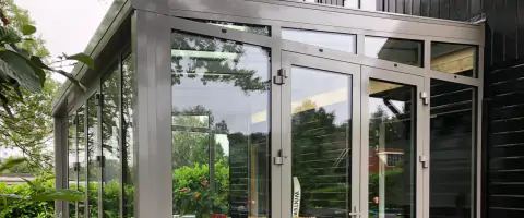 Een serre met een tafel en stoelen, omringd door glazen wanden en een stolpdeur.