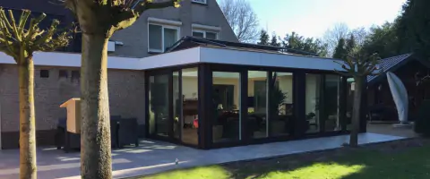 Een woning met een ruim terras en grasveld, inclusief zwarte palen aanbouw serre en lichtstraat.