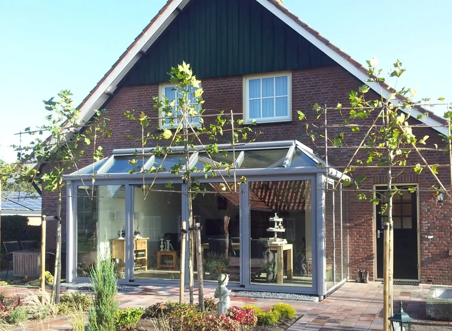 Aluminium serre met glazen dak en knikconstructie als aanbouw aan een woning