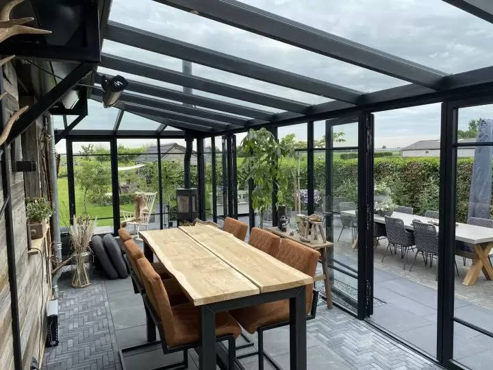 Binnenaanzicht van zwarte stoollook serre met stolpdeuren naar buiten en lessenaars dak. Voorbeeld hoe een tuinkamer inrichten
