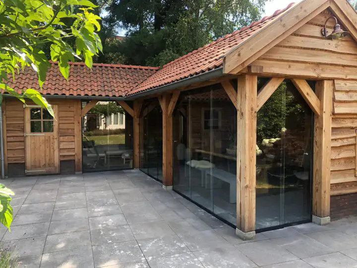 Hardglazen schuif- en vouwdeuren in houten tuinkamer met puntdak