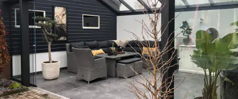 Een huiselijke patio met een tafel en stoelen. Tuinkamer met zadeldak en schuifwand.