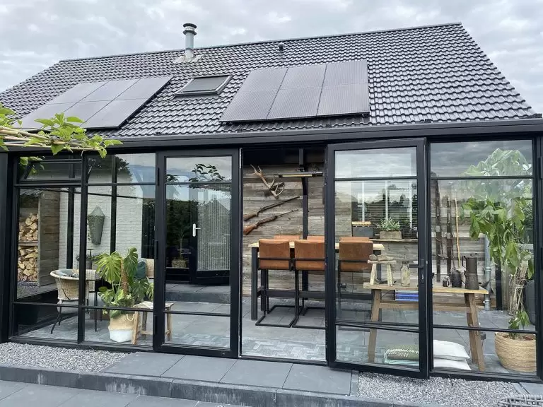 Zwarte serre aanbouw met plat dak en openslaande stolpdeuren